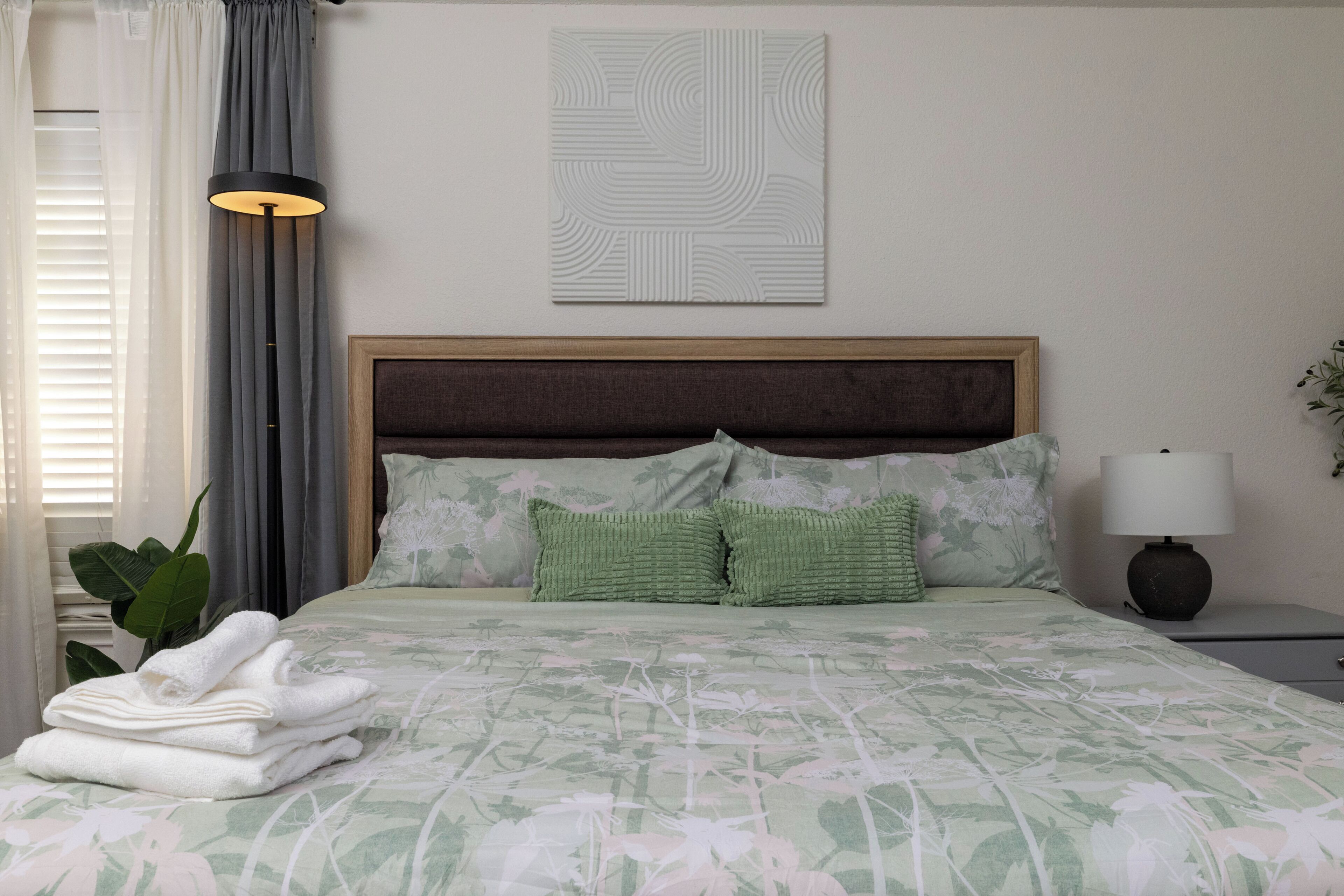 A neatly made bed with floral bedding, a headboard, and a bedside lamp.