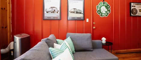A room with a red wall, a grey sofa, and two framed car posters.