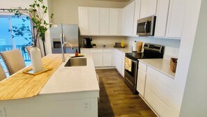 Una cocina moderna con armarios blancos, un refrigerador de acero inoxidable, un microondas y una encimera de madera.