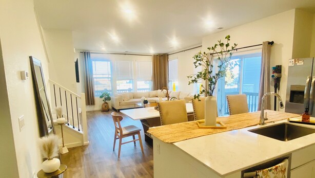 Una cocina moderna con una isla central, una zona de comedor con sofá y sillas, y una sala de estar con un sofá y una mesa baja.