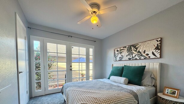 Un dormitorio con cama, mesita de noche, ventilador de techo y un amplio ventanal con vistas al exterior.