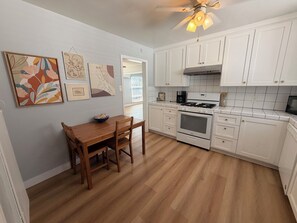 Una cocina con armarios blancos, una mesa de comedor de madera y un ventilador de techo.