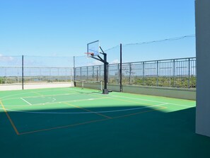 An outdoor basketball court with a netted enclosure, a basketball hoop, and a clear view of the surrounding landscape. - Palisades Palms Tw1012 - Sea Escape (Galveston)