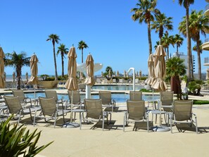 A poolside area with lounge chairs and umbrellas, palm trees, and a clear view of the ocean. - Palisades Palms Tw1012 - Sea Escape (Galveston)