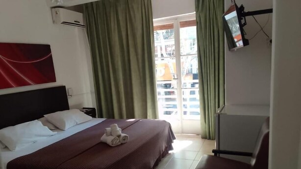A hotel room with a bed, a chair, a TV, and a window with curtains. - Gran Hotel Turismo (Mendoza)
