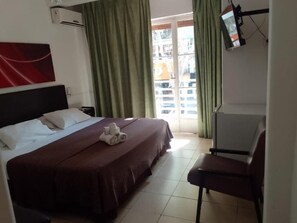 Une chambre d’hôtel avec un lit, une chaise, une télévision et une fenêtre avec des rideaux.