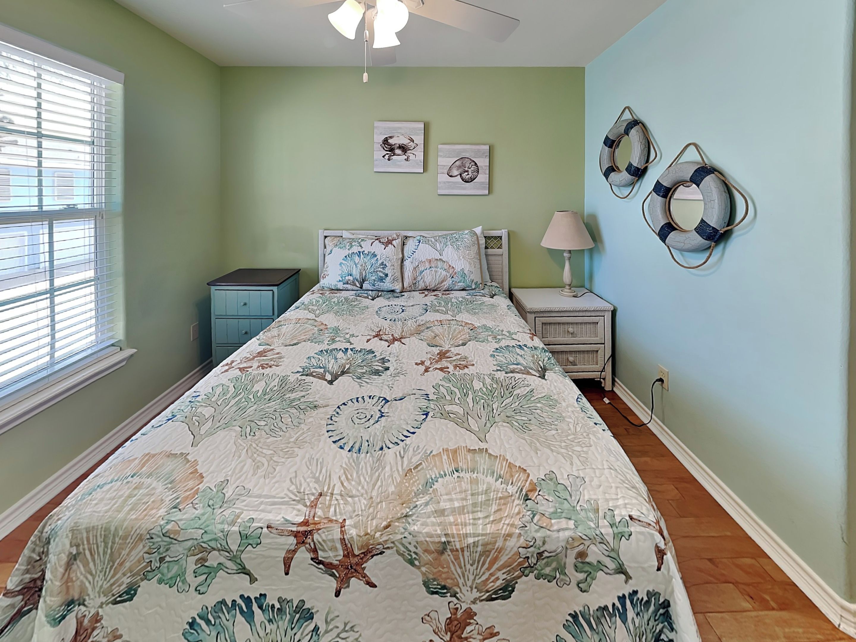 A bedroom with a bed, nightstands, a lamp, and wall decorations including framed pictures and life rings.