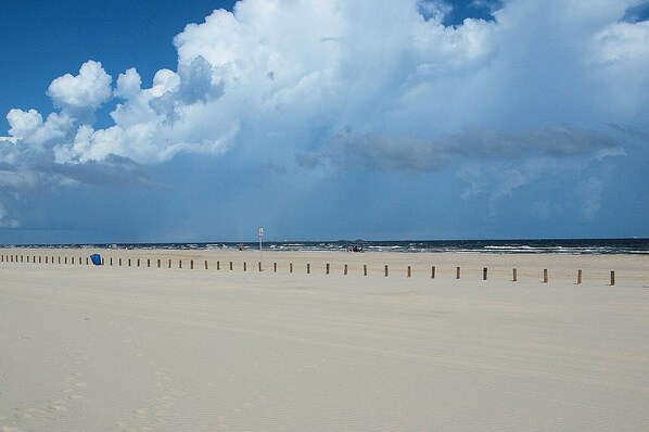 A beach with a wooden fence and a sign, under a partly cloudy sky. - Sandy Seashell (Port Aransas)