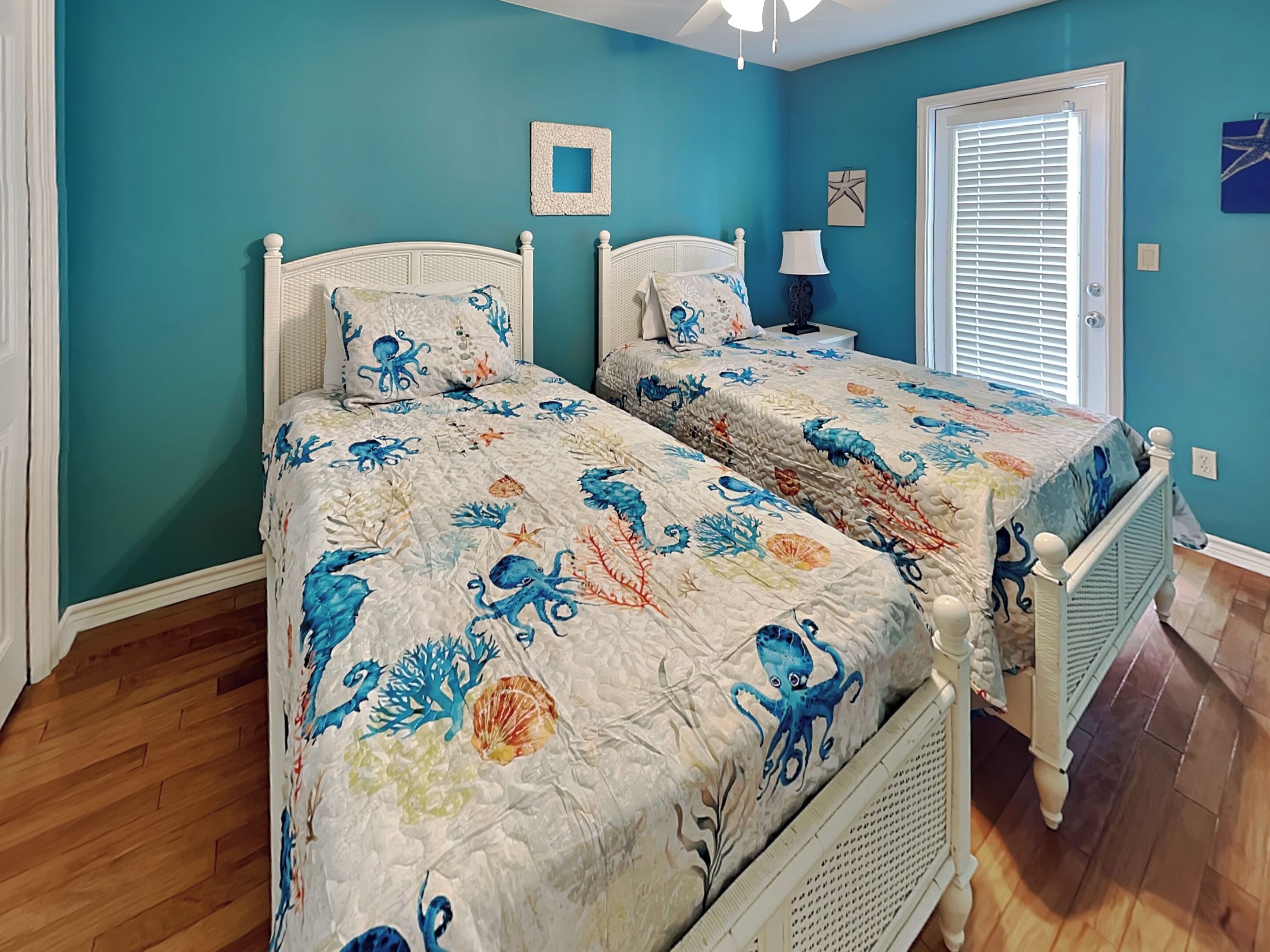 A bedroom with two beds, teal walls, and a wooden floor.