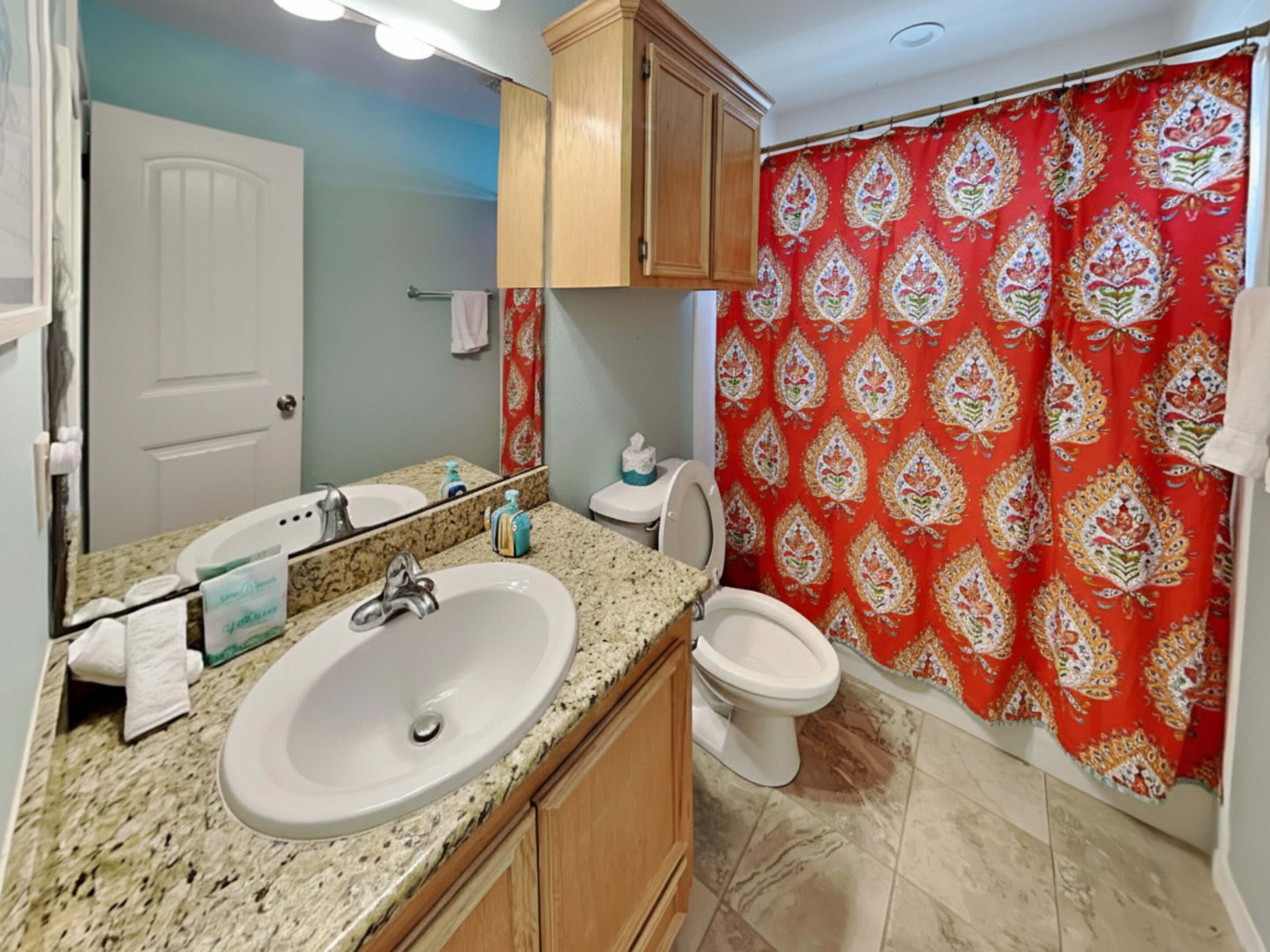 A bathroom with a granite countertop sink, a mirror, a toilet, and a shower curtain with a floral pattern.