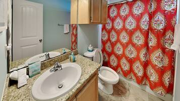A bathroom with a granite countertop sink, a mirror, a toilet, and a shower curtain with a floral pattern.