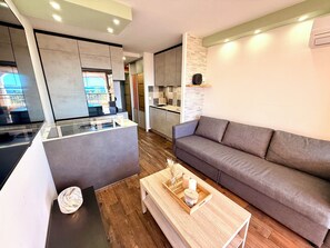 A modern living area with a sofa, a coffee table with candles, and a kitchen in the background. - Le Panoramique Cap Esterel sea view (Saint-Raphaël)