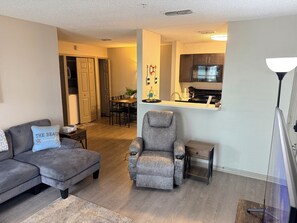 A living room with a sofa, armchair, and a small table. There is a kitchen area with a microwave and cabinets. - Lux Pool Home, Mins to Mayo, Beach, UNF and Spine& Pain (Jacksonville)