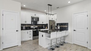 A modern kitchen with white cabinetry, a black backsplash, stainless steel appliances, and a central island with bar stools. - Downtown Houston escape with en-suites (Houston)