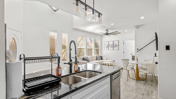 A modern kitchen with a black countertop, stainless steel sink, and a built-in oven. There is a dining area with a white table and chairs, and a ceiling fan. - Downtown Houston escape with en-suites (Houston)