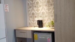 Eine kleine Küche mit Kühlschrank, Kaffeemaschine und Feuerlöscher.