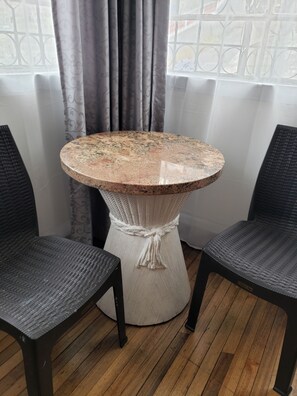 A round table with a textured top, flanked by two dark wicker chairs, set against a window with patterned curtains. - SUIT WITH THE BEST VIEW OF THE HISTORIC CENTER OVERLOOKING THE PANECILLO (Quito)