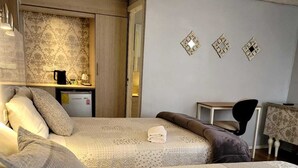 Ein Hotelzimmer mit zwei Betten, einem Schreibtisch, einem Stuhl und einer kleinen Küchenzeile.