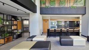 A modern hotel lobby with a mezzanine level, seating areas, and a kitchenette. - COBAR0144 - Edifício Único Barra (Salvador)
