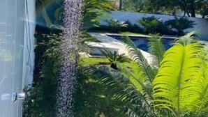 A vertical water feature with a cascading effect, surrounded by lush greenery and palm trees. - Pousada Villa Novo Tempo  (Guarujá)