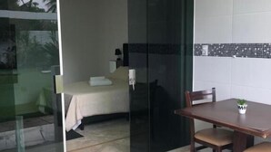 A room with a bed, a table with chairs, and a sliding glass door leading to an outdoor area. - Pousada Villa Novo Tempo  (Guarujá)
