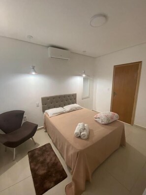 Ein Schlafzimmer mit einem Bett, einem Sessel, einem kleinen Teppich und einer Tür.