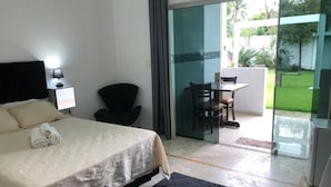 A hotel room with a bed, a desk, and a chair near a sliding glass door leading to a balcony with a view of greenery. - Pousada Villa Novo Tempo  (Guarujá)