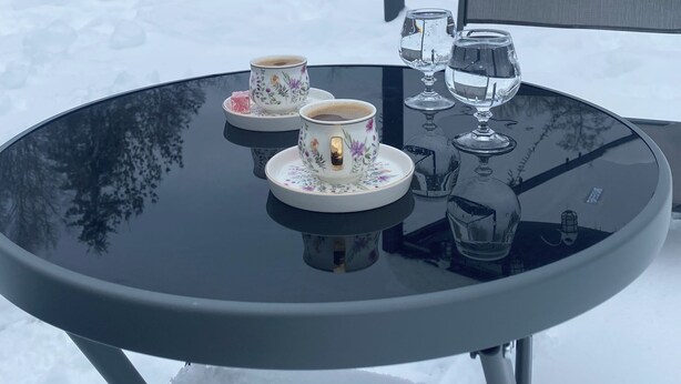 Ein runder Tisch mit zwei Tassen und einem Glas, draußen in verschneiter Landschaft.