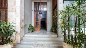 Un hall d’entrée au sol en pierre, avec une porte en bois, des plantes en pot et un paillasson vert.
