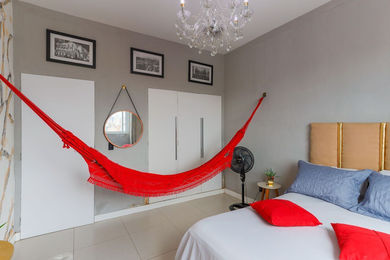 Un dormitorio con cama, una hamaca roja, ventilador, candelabro y cuadros en la pared.