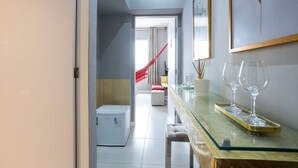 Une chambre d’hôtel moderne avec une table basse en verre, un petit réfrigérateur et, au fond, un hamac rouge.