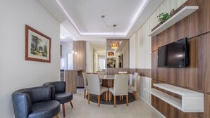 Een moderne woonkamer met een bank, eettafel, stoelen, een televisie en een keuken op de achtergrond.
