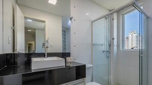 Een moderne badkamer met een zwarte wastafel, een witte wasbak en een douche met glazen wanden.