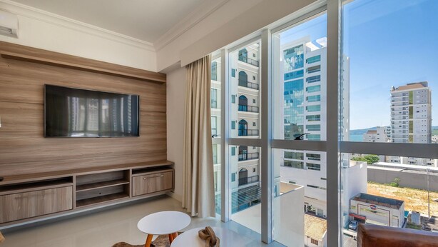 Een moderne woonkamer met een grote televisie, een houten dressoir en uitzicht op hoge gebouwen.