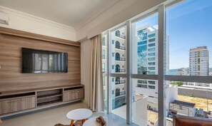 Una sala de estar moderna con un televisor grande, un mueble de madera para entretenimiento y vistas a rascacielos.