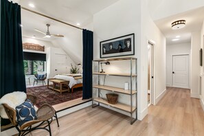 Quarto moderno com cama, escrivaninha e cadeira. Há uma janela com cortinas, um ventilador de teto e uma moldura com um quadro na parede.