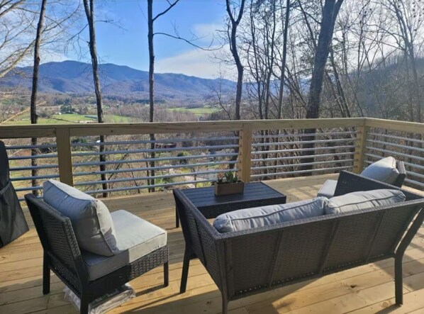 A wooden deck with wicker furniture, a table, and a view of mountains and a valley.