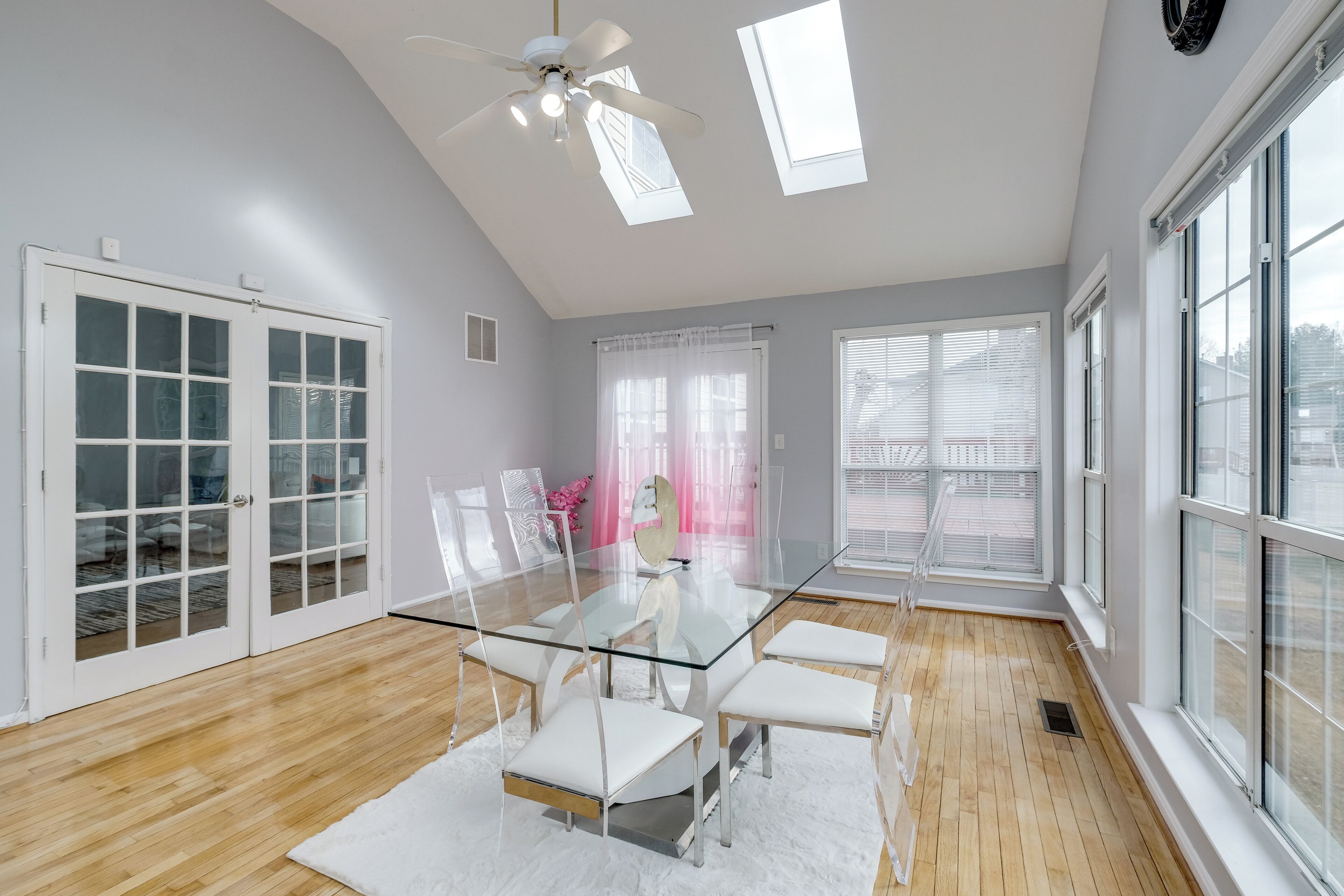 A modern dining room with a glass table, white chairs, and a ceiling fan.