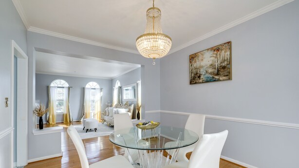 A dining area with a glass table, white chairs, a chandelier, and a painting on the wall. - 'The Mirror' - Elegant & Dog-Friendly DMV Home (Upper Marlboro)