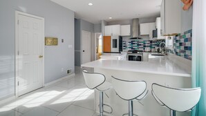A modern kitchen with white cabinets, a tiled backsplash, and a central island with bar stools. - 'The Mirror' - Elegant & Dog-Friendly DMV Home (Upper Marlboro)