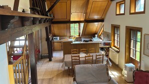 Eine geräumige Küche mit Holzbalken, einem Essbereich mit Tisch und Stühlen sowie Blick ins Freie durch große Fenster.
