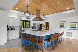 A modern kitchen with white cabinetry, a large island with bar stools, and a wooden ceiling. - Mtn Views + Theater + Hot Tub | 5 King Suites (Blue Ridge)