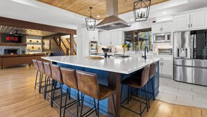 Een moderne keuken met witte kasten, roestvrijstalen apparatuur en een groot eiland met barstoelen.