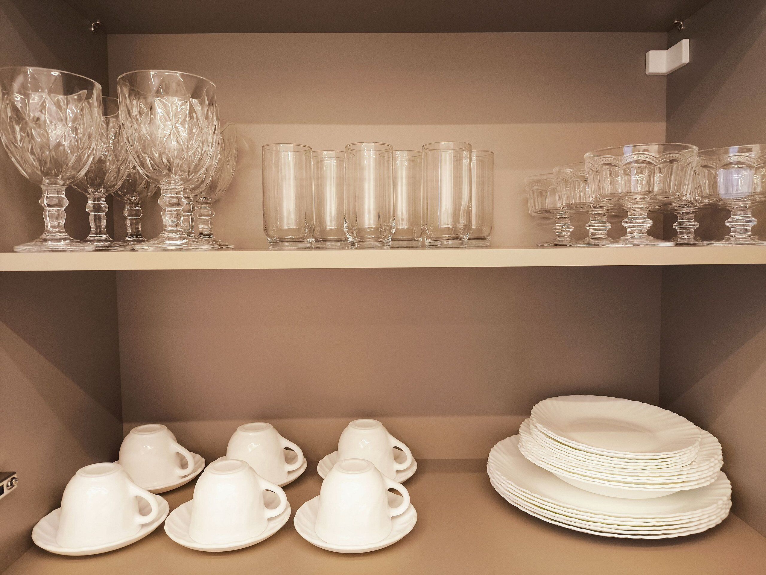 A shelf with various glassware and white ceramic cups and saucers.