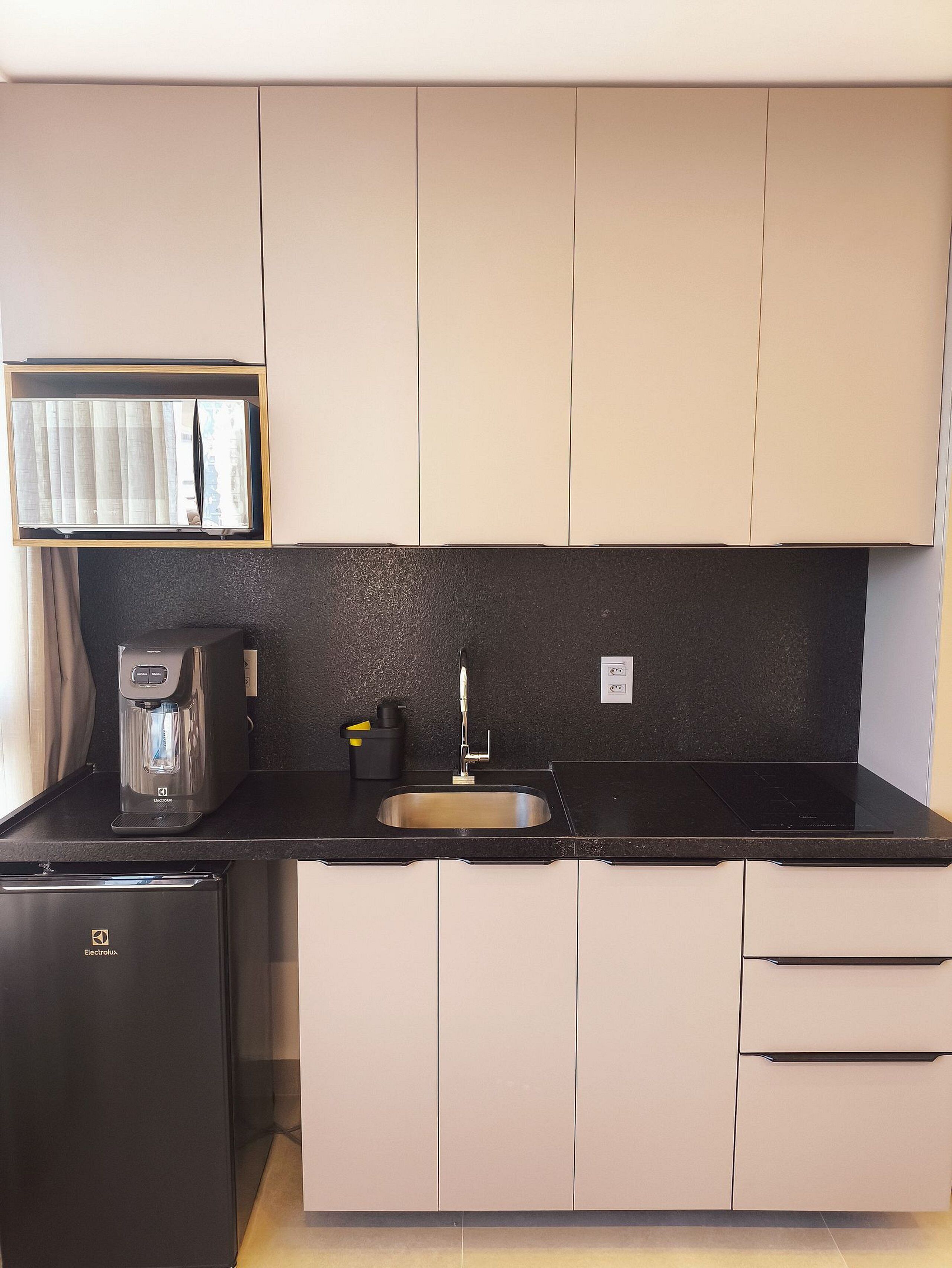 A compact kitchen with a built-in refrigerator, a coffee maker, and a sink.