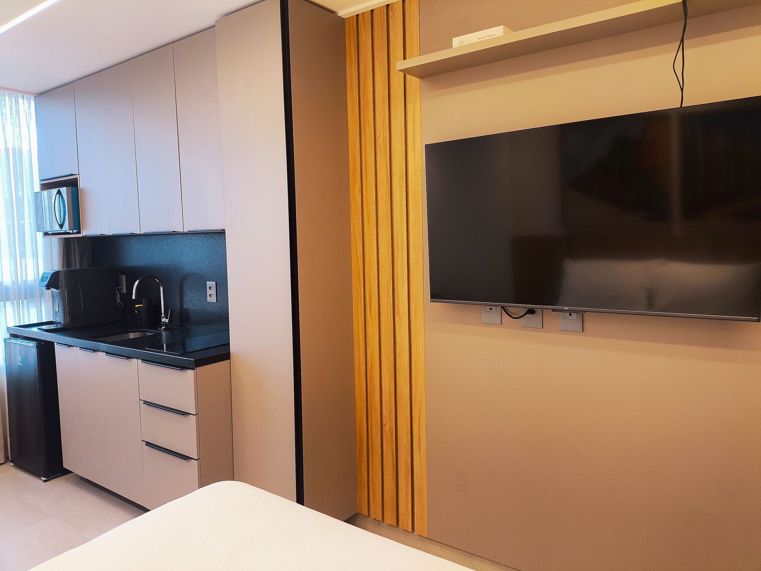 Una cocina moderna con microondas incorporado, cafetera y televisor de pantalla plana montado en la pared.