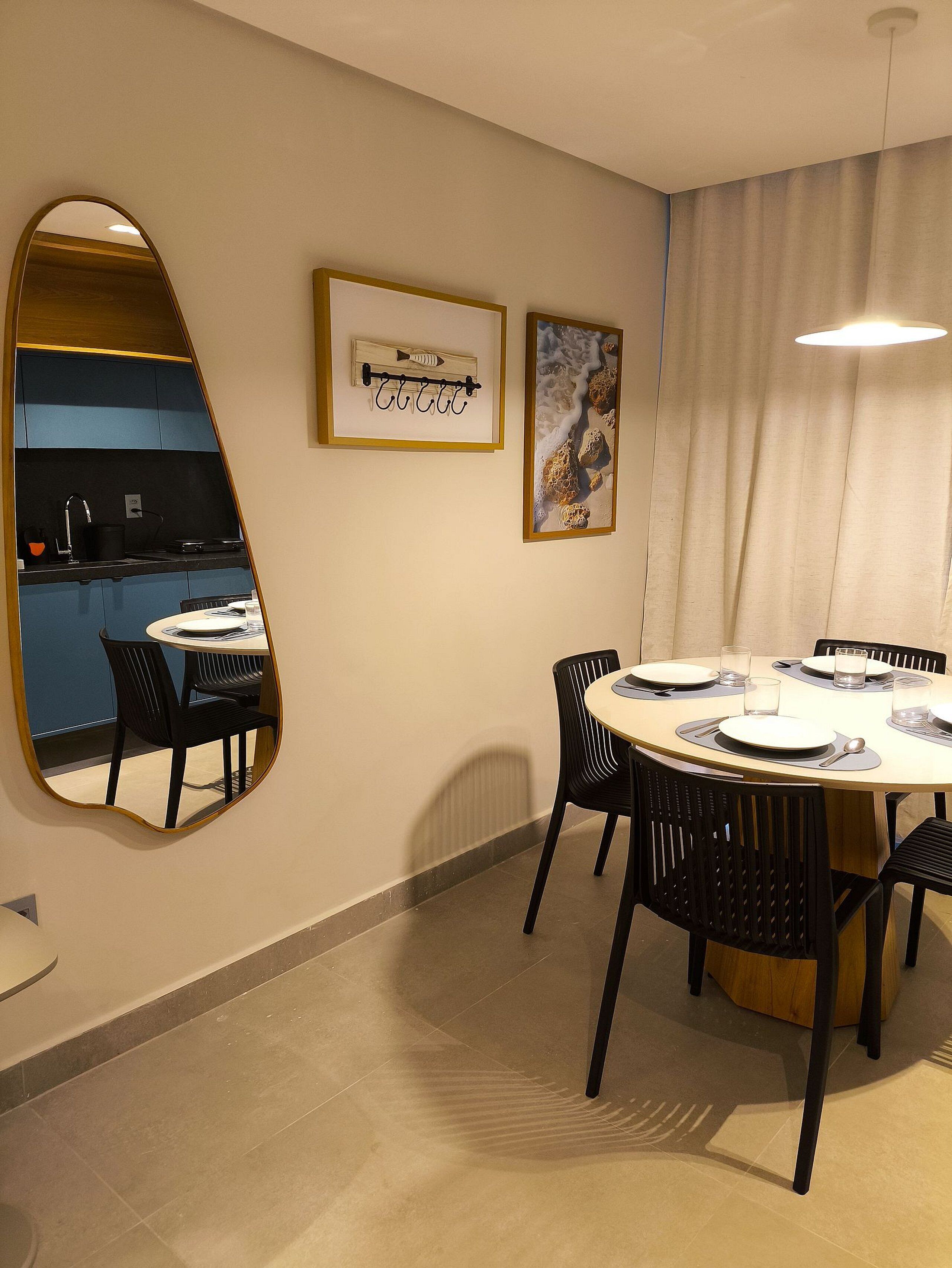Un comedor con una mesa redonda, sillas negras, una cocina al fondo y un espejo en la pared.
