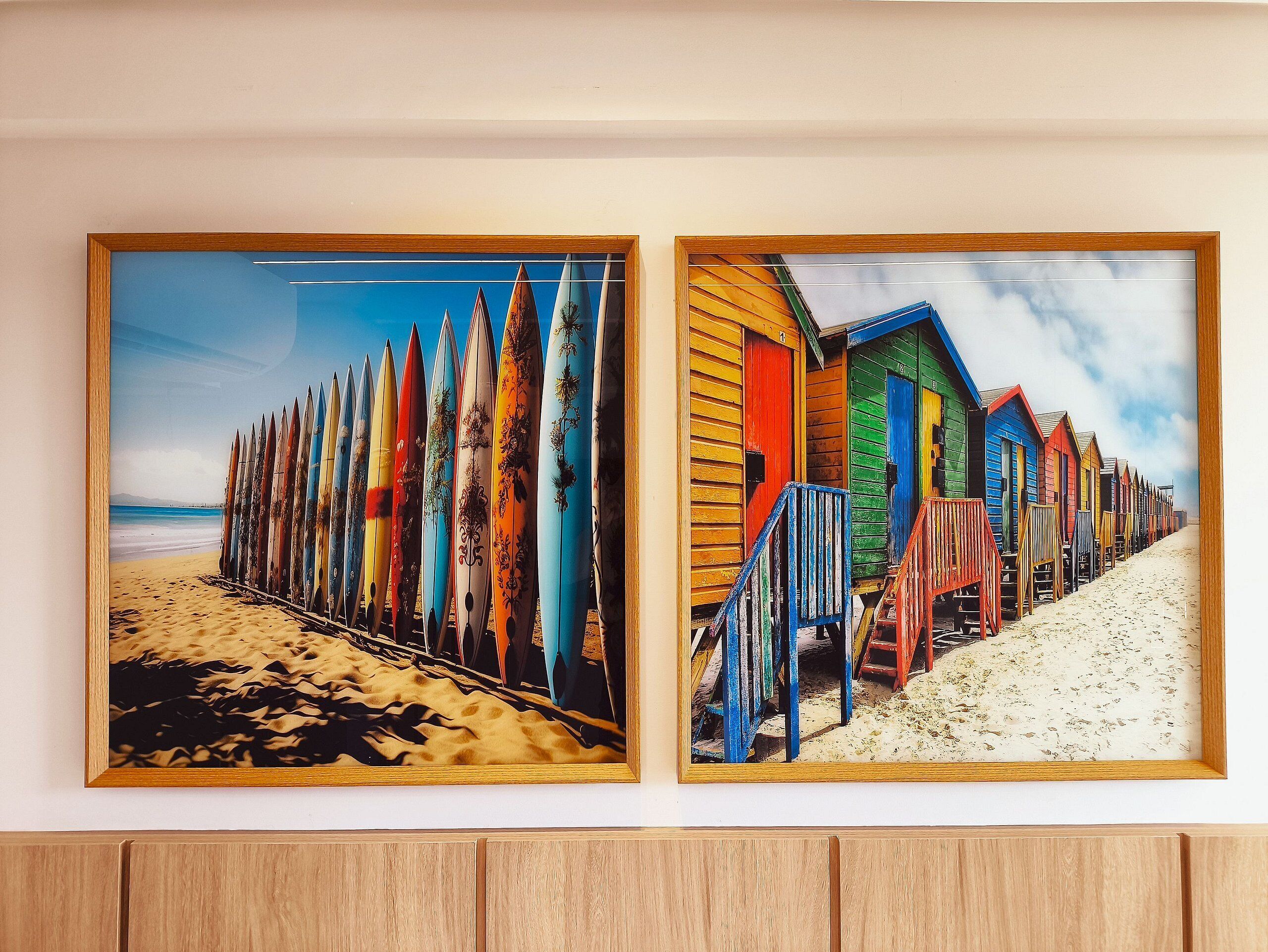 Two framed pictures of a beach scene with colorful beach huts and surfboards.