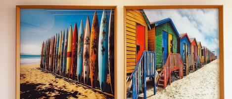 Two framed pictures of a beach scene with colorful beach huts and surfboards.