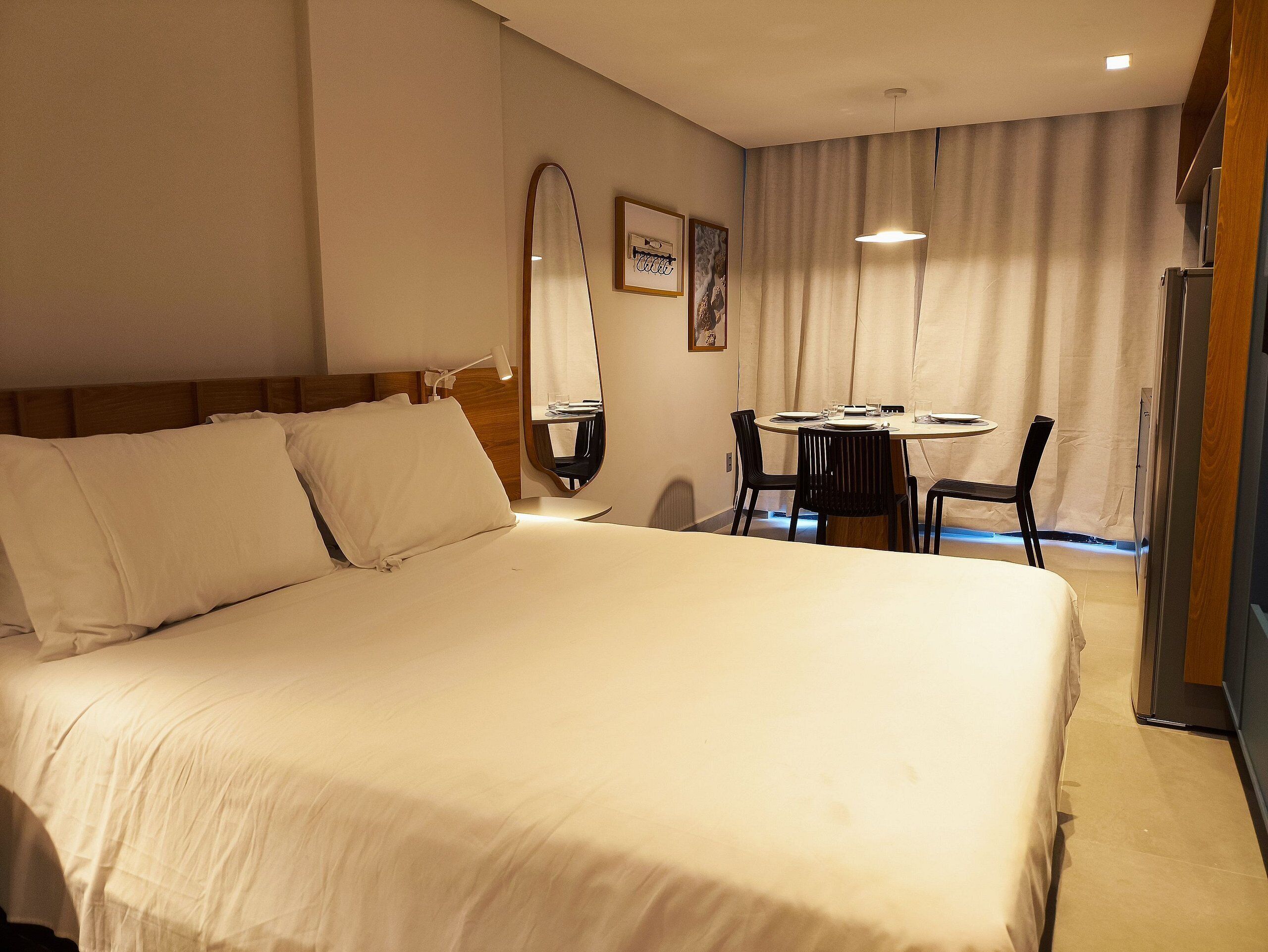 A hotel room with a large bed, a small round table with chairs, a mirror, and a television.